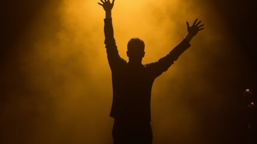 Silhouette of a performer on a dark stage under a golden spotlight with arms raised in triumph