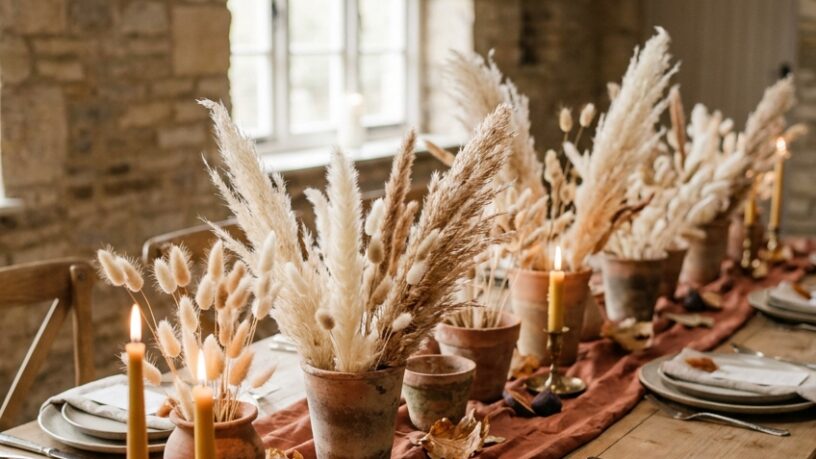 Rustic fall wedding table with terracotta pots of dried grass and lit brass taper candles