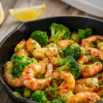 Garlic butter shrimp and broccoli skillet in a cast iron pan, garnished with parsley and red pepper flakes with lemon wedges alongside.