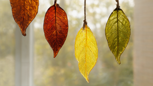 Hot glue faux stained glass fall leaf suncatchers in amber, rust, yellow and olive green hanging on a sunny window.