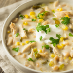 A bowl of creamy white chicken chili with shredded chicken, cannellini beans, corn and green chiles, topped with Greek yogurt and cilantro.