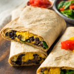 Two make-ahead black bean and egg breakfast burritos sliced in half on a rustic wooden board with salsa