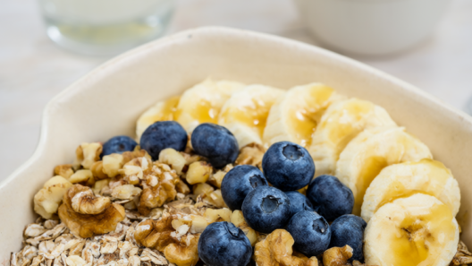 Healthy breakfast bowl of rolled oats topped with blueberries, banana and walnuts beside milk and plain yogurt.