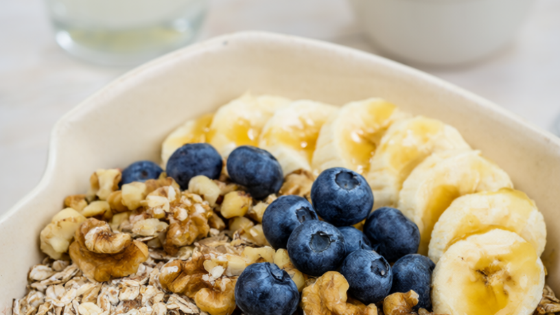 Healthy breakfast bowl of rolled oats topped with blueberries, banana and walnuts beside milk and plain yogurt.
