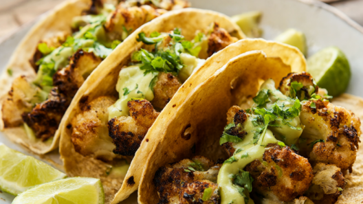 Three crispy roasted cauliflower tacos with avocado crema, cilantro and lime wedges