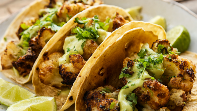 Three crispy roasted cauliflower tacos with avocado crema, cilantro and lime wedges