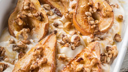 Honey roasted pear halves topped with toasted walnuts and Greek yogurt in a white baking dish