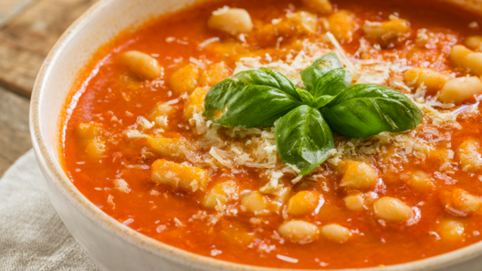 Bowl of creamy tomato white bean soup topped with fresh basil and grated Parmesan on a rustic wooden table