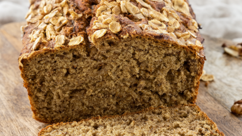 Sliced healthy banana bread with Greek yogurt and oats topped with walnuts on a rustic wooden board