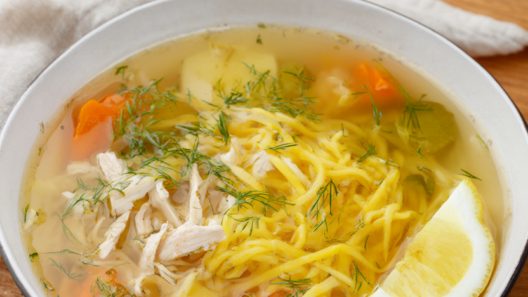 A bowl of 45-minute chicken noodle soup with shredded chicken, egg noodles, carrots and celery, garnished with fresh dill and a lemon wedge.