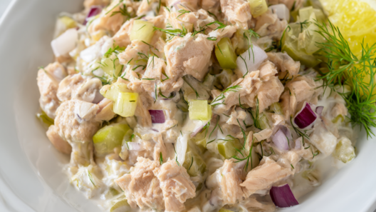No-mayo tuna salad with Greek yogurt, celery and pickles in a white bowl on a light wood table