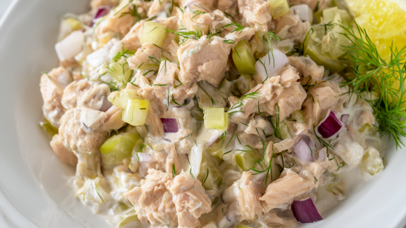 No-mayo tuna salad with Greek yogurt, celery and pickles in a white bowl on a light wood table