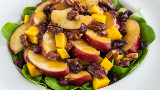 Apple pecan salad with sliced apples, cheddar, toasted pecans and dried cranberries over baby spinach on a white platter