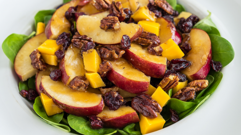 Apple pecan salad with sliced apples, cheddar, toasted pecans and dried cranberries over baby spinach on a white platter