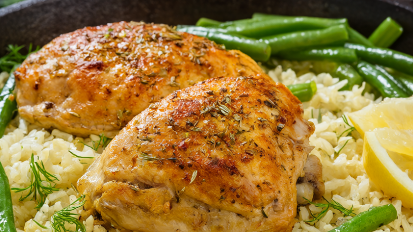 Golden seared Greek chicken thighs baked on lemon-garlic rice with green beans in a skillet