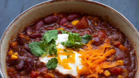 A steaming bowl of hearty beef and bean chili topped with sour cream, cheddar and cilantro.
