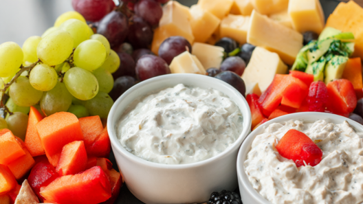 Healthy party snack board with raw vegetables, grapes, berries, cheese, almonds, whole-grain crackers and two bowls of dip.