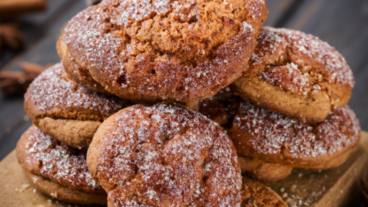 Chewy gingerbread cookies with crackled sugar tops stacked on a rustic wooden board with cinnamon sticks and star anise