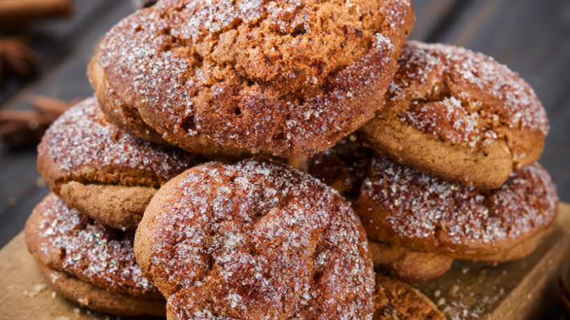Chewy gingerbread cookies with crackled sugar tops stacked on a rustic wooden board with cinnamon sticks and star anise