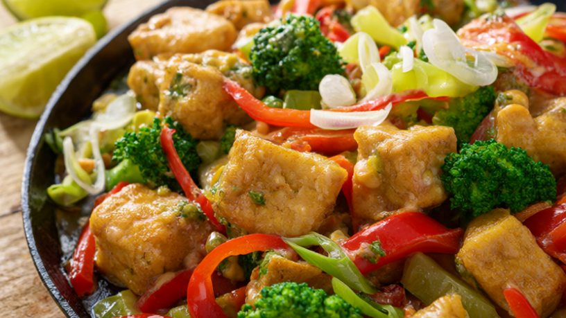 Crispy peanut tofu stir fry with broccoli and red bell pepper in a cast-iron skillet