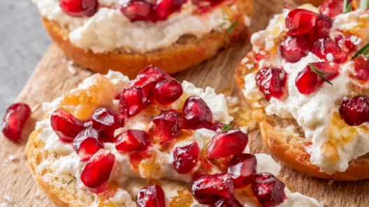 Pomegranate ricotta crostini topped with ruby-red pomegranate arils, honey drizzle and fresh rosemary