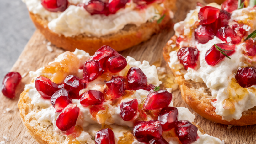 Pomegranate ricotta crostini topped with ruby-red pomegranate arils, honey drizzle and fresh rosemary