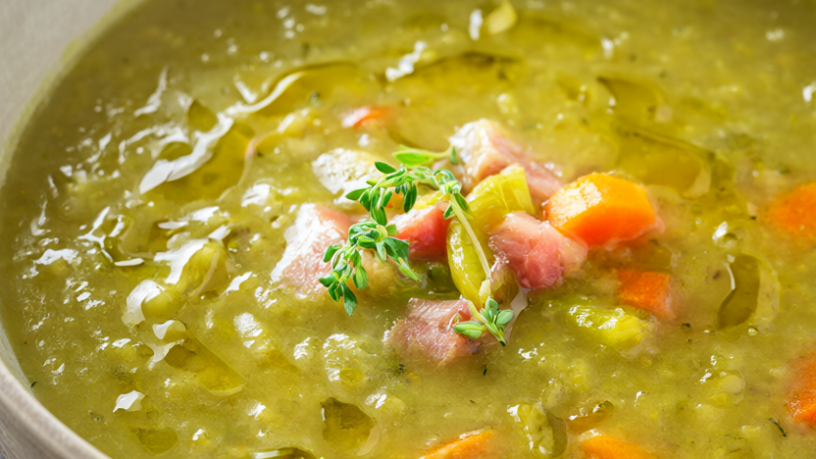 Rustic bowl of green split pea soup with ham, carrots, and celery, garnished with fresh thyme
