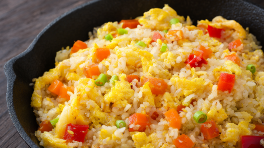 Cauliflower fried rice with scrambled egg, carrots, bell pepper, and scallions in a black cast-iron skillet.