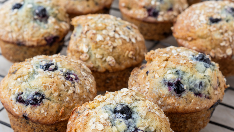 Golden blueberry oatmeal muffins with bursting blueberries on a wire cooling rack
