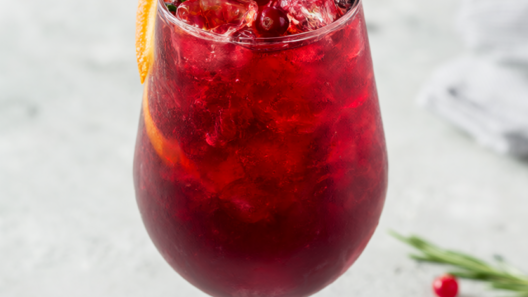 Sparkling cranberry mocktail in a tall glass with rosemary, cranberries and an orange slice