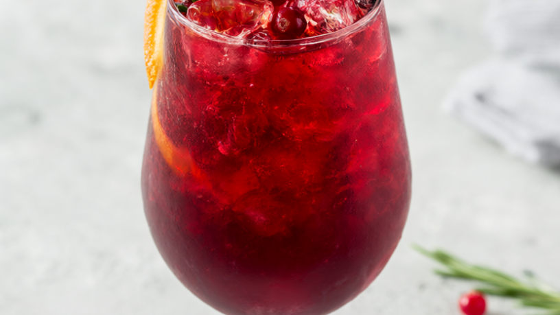 Sparkling cranberry mocktail in a tall glass with rosemary, cranberries and an orange slice