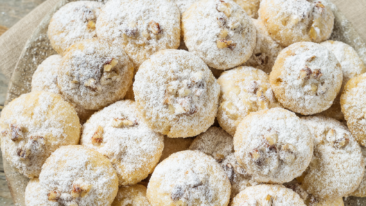Buttery pecan snowball cookies rolled in powdered sugar on a rustic wooden table