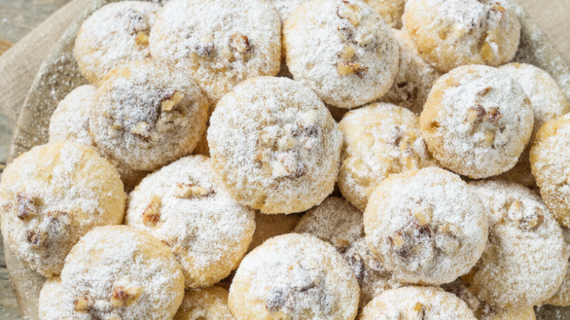 Buttery pecan snowball cookies rolled in powdered sugar on a rustic wooden table