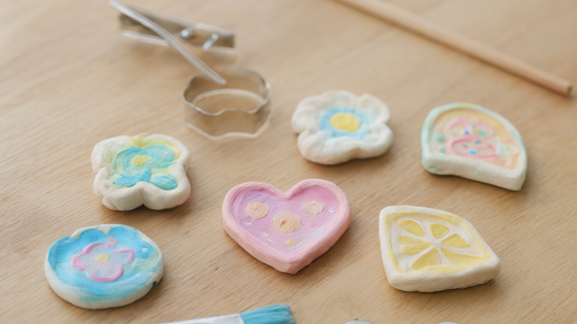 Finished pastel air-dry clay fridge magnets in flower, heart and citrus-slice shapes with painted details on a light oak craft table