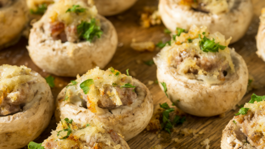 Baked sausage stuffed mushrooms with golden Parmesan tops and fresh parsley on a rustic wooden serving board.