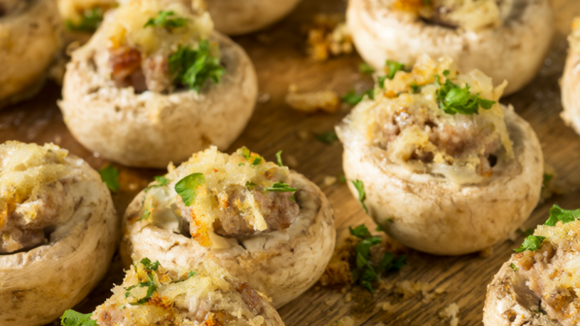 Baked sausage stuffed mushrooms with golden Parmesan tops and fresh parsley on a rustic wooden serving board.