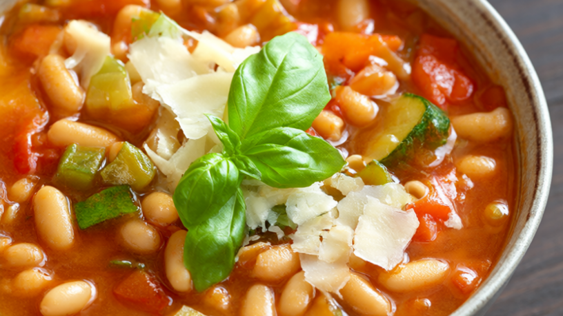 Bowl of minestrone soup with cannellini beans, zucchini, carrots, celery and ditalini pasta topped with basil and parmesan