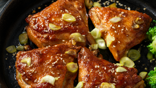 Golden glazed honey garlic chicken thighs with scallions and sesame seeds in a cast-iron skillet