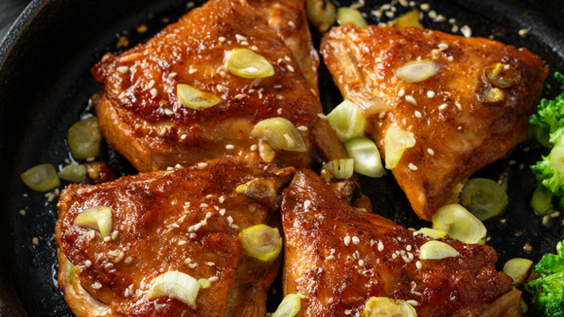 Golden glazed honey garlic chicken thighs with scallions and sesame seeds in a cast-iron skillet