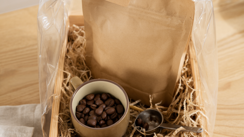Finished DIY coffee gift basket in a wooden crate with a coffee bag, ceramic mug, espresso beans, kraft filler and a jute twine bow, on a kitchen counter