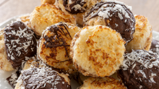 Golden coconut macaroons on a white plate, several dipped in dark chocolate.