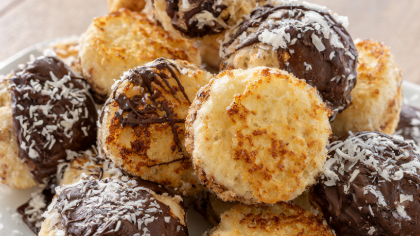 Golden coconut macaroons on a white plate, several dipped in dark chocolate.