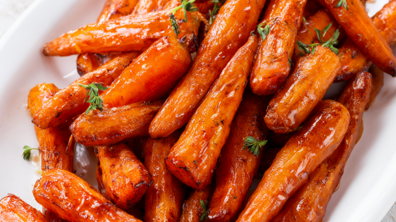 Maple roasted baby carrots in a glossy maple butter glaze with fresh thyme on a white platter