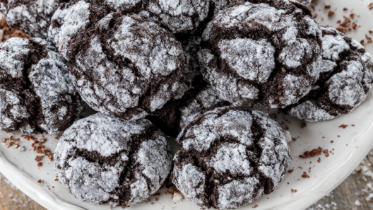 A pile of chocolate crinkle cookies with crackled powdered-sugar tops on a white ceramic plate