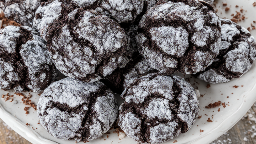 A pile of chocolate crinkle cookies with crackled powdered-sugar tops on a white ceramic plate