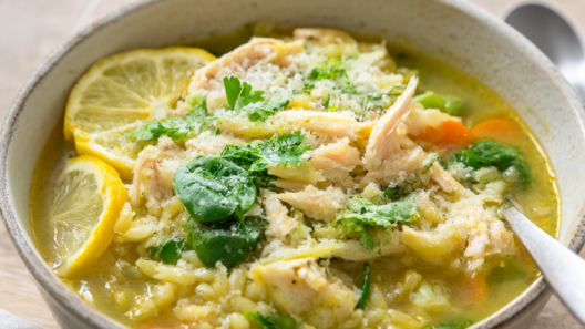 Overhead view of crockpot lemon chicken orzo soup with shredded chicken, spinach, carrots, celery and orzo in a bright lemony broth topped with Parmesan and lemon slices.