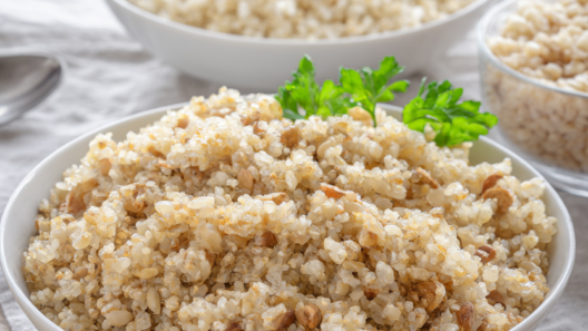 Three bowls of freshly cooked quinoa, brown rice and farro garnished with parsley on a wooden table