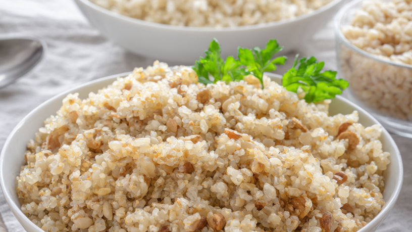 Three bowls of freshly cooked quinoa, brown rice and farro garnished with parsley on a wooden table