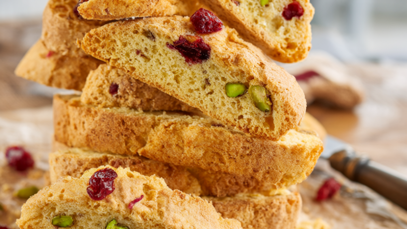 Stacked pistachio and cranberry biscotti on a rustic wood board over parchment.