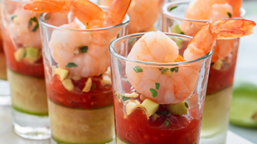 A platter of shrimp cocktail cups: cucumber rounds filled with cocktail sauce, poached shrimp, avocado and chives.